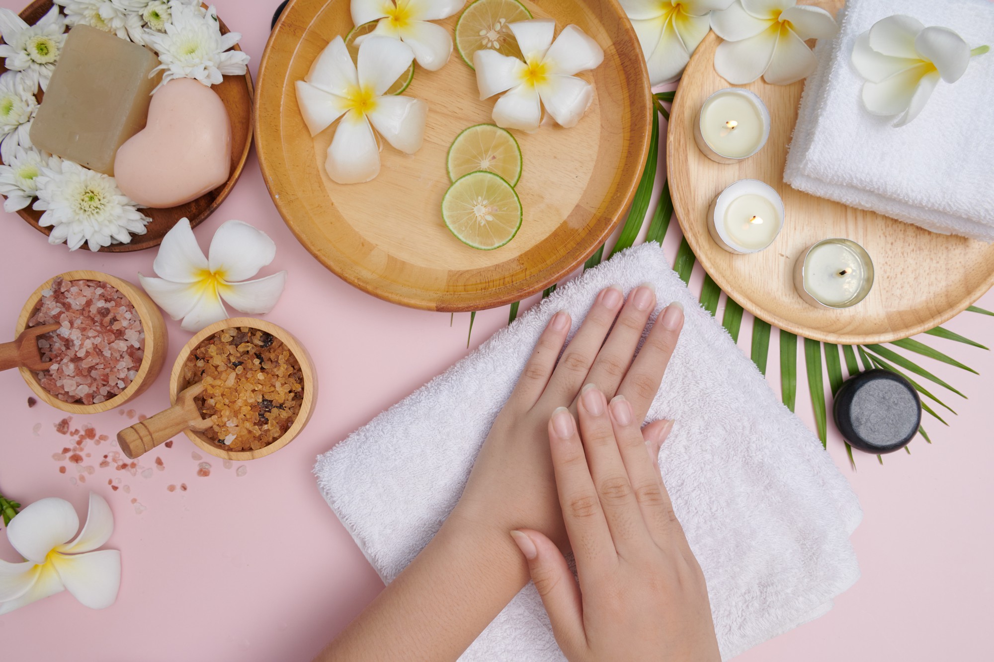 young woman applying natural scrub hands against pink surface spa treatment product female hand spa massage perfumed flowers water candles relaxation flat lay top view